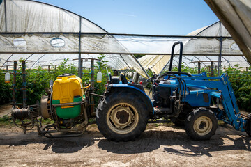 Obraz premium Blue tractor fitted with a yellow and green sprayer, parked outside a row of greenhouse raspberries under a clear sunny sky. Longueira-Almograve, Portugal.