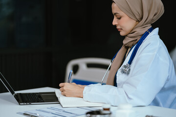 Doctor woman sitting at table and writing on a document report in hospital office. Medical...