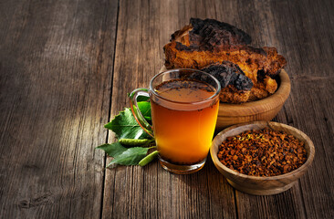 Chaga mushroom pieces and chaga mushroom tea with birch leaves on a wooden background.