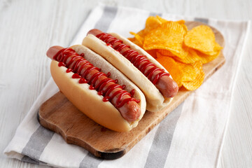 Homemade Hot Dog with Ketchup with Potato Chips on a Wooden Board, side view.