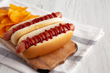 Homemade Hot Dog with Ketchup with Potato Chips on a Wooden Board, side view.