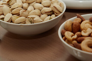 Plates with different nuts on a table, pistachios, almonds and cashews in bowls, finger food