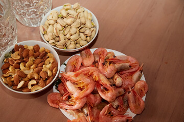 Pistachios, almonds, cashews and boiled shrimp on a table next to beer glasses, close-up, bar snacks