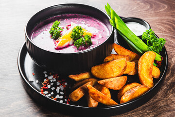 Vibrant beetroot soup with cream, herbs, and roasted potato wedges on a wooden table
