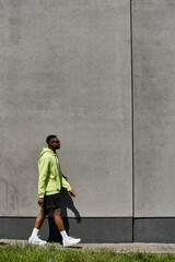 A fashionable young African American man walking in front of a gray wall.