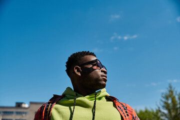 Handsome African American man in green hoodie gazes up at the sky.