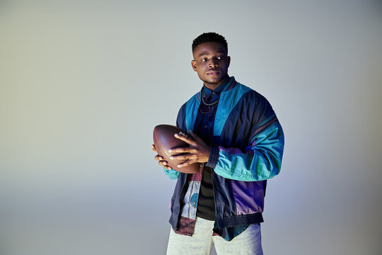 African American man in fashionable attire holding a football. - Powered by Adobe