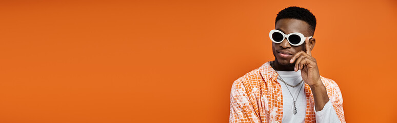 Handsome African American man in trendy sunglasses on vibrant orange background.