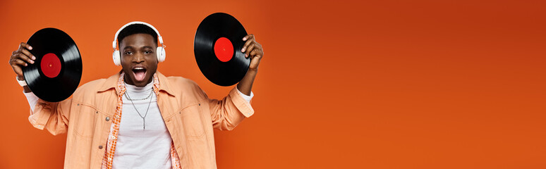 Man holding two vinyl records against an orange backdrop.
