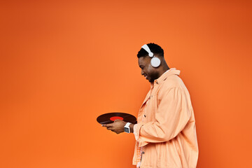 Handsome African American man in headphones holds record on orange backdrop.