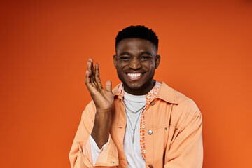 A young man in an orange jacket confidently poses for the camera.
