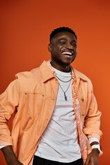 Handsome man in orange jacket smiling against orange backdrop.