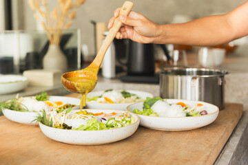 Woman hand pouring sauce into Thai rice noodles dish on table.