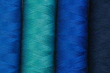 Various spools of blue and green yarn neatly arranged in a row