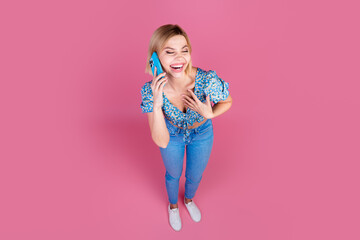 Full size high angle view photo of pretty young girl speak phone laugh wear top isolated on pink color background