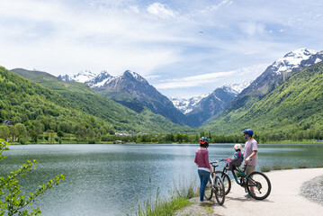 Family spending a nice spring day with their bikes around a beautiful lake surrounded by mountains in Louron Valley, french pyrenees.