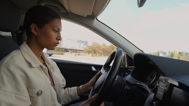 Medium shot of concentrated female African American student sitting in learners car adjusting steering wheel before starting driving session