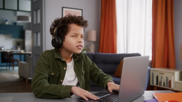 African American ethnic little boy child kid son gamer user playing online internet game laptop computer pc gaming play at home in headphones lost failure bad result sad upset reaction addiction fail
