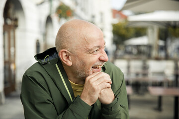Cheerful Elderly Man in Green Jacket Laughing at Urban Cafe Setting