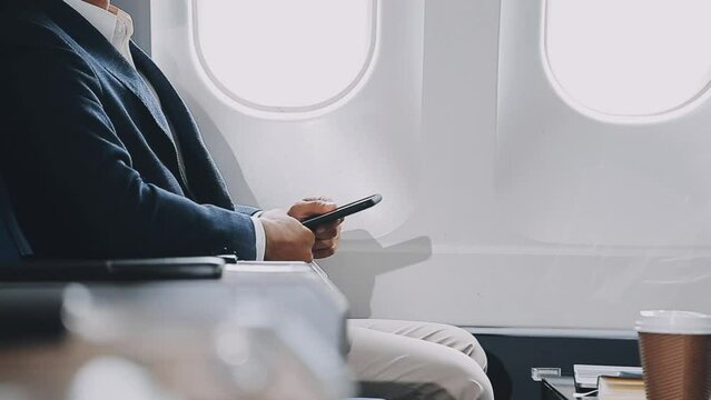 successful asian businessman in suit and glasses sits in private jet and uses smartphone, korean entrepreneur flies in an airplane and types on the phone online