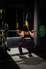 A woman is performing a squat exercise with a barbell at the gym