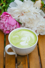 A cup of matcha latte with peony flowers on the background