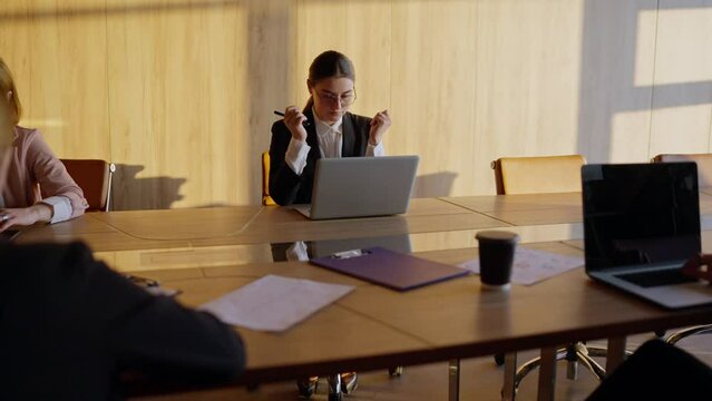A tired girl in round glasses and a business uniform a businesswoman, sits at the table and tries to relax during a hard day at work with her colleagues - Powered by Adobe