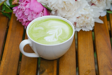 A cup of matcha latte with peony flowers on the background