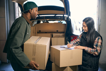 Young couple is holding boxes while standing near a car with an open trunk