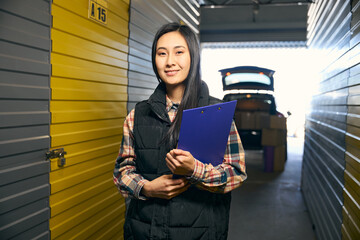 Successful woman holding blue folder in her hands while standing in a warehouse