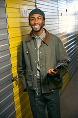 Smiling African man stands in storage service and holds a folder in his hands