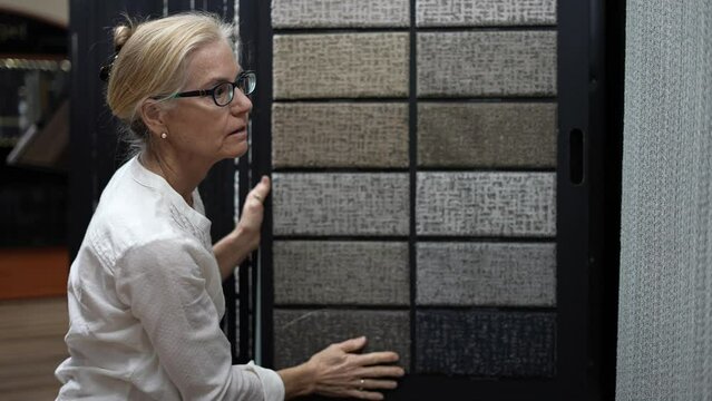 Closeup of mature woman hand touching carpet samples while looking through other samples for home redecorating project, in a design center floor store.