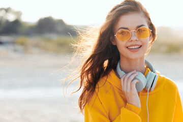 Joyful woman in yellow sweater and sunglasses holding headphones with a smile