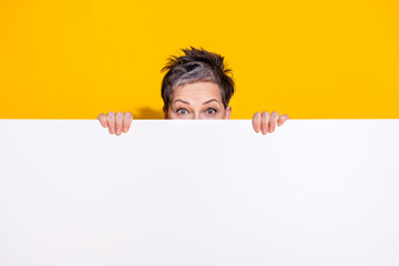 Portrait of nice aged lady hide behind empty space wear t-shirt isolated on yellow color background