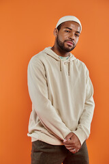 Stylish African American man posing in front of vibrant orange backdrop.