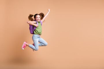 Photo of positive girl kid jump hold rucksack raise win fist up empty space isolated pastel color background