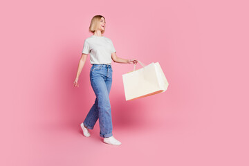 Full size photo of adorable woman dressed white t-shirt holding shopping bags walk look empty space...