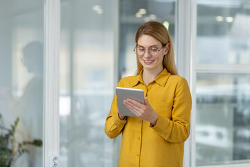Smiling woman using a tablet in a bright, modern office environment. Ideal for business, technology, and workplace concepts.