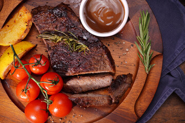 Food: Grilled steak, tomatoes, lemon and rosemary on a European and American style wooden plate.