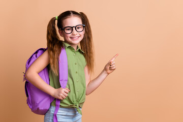 Photo of positive girl kid point finger copyspace hold rucksack isolated pastel color background