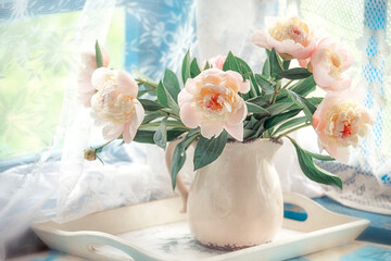 A bouquet of pale pink peonies in a vase by an old window on the terrace. light gentle photo.