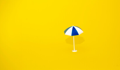 Beach relaxation and vacation concept. Toy sun blue umbrella on yellow colorful paper background.