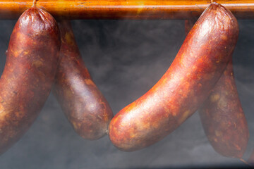 Smoked sausages hanging on rack in a smokehouse with a thick smoke, closed up