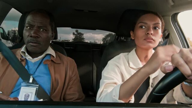 Medium of young Biracial woman driving left-handed car under supervision of instructor, listening to directions, honing her skills before passing test and obtaining license