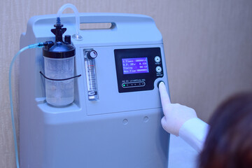 A hand in a medical glove turns on an oxygen generator concentrator to deliver at low lung oxygen saturation for Covid-19 pneumonia, asthma and other diseases. Rescue during the coronavirus epidemic