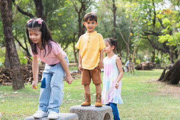 Group of multiracial children in line to jumping from stone chair to another one chair outdoors in...