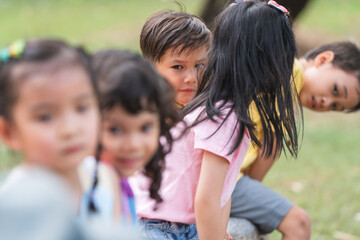 Group of multiracial children smiling, sitting at stone chair, playing together outdoors in summer park. Adorable kids have fun playing in playground. Selective focus on a boy