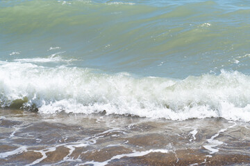 Fototapeta premium Beautiful blue sea and large calm waves and foam. Wave splashing over pebbles at sea. Rolling ocean waves. Summer paradise beach background. Powerful sea waves