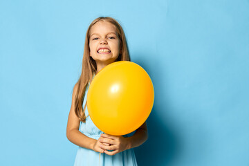 Young girl holding a bright yellow balloon against a vibrant blue backdrop, capturing a moment of...