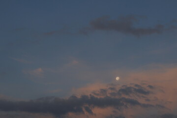 Una toma de lejos de una luna entre nubes en el cielo al amanecer